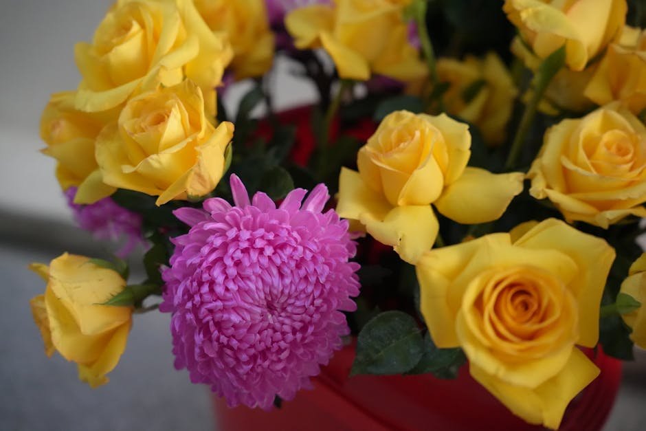 A close-up of vibrant yellow roses paired with a pink chrysanthemum in a bouquet.