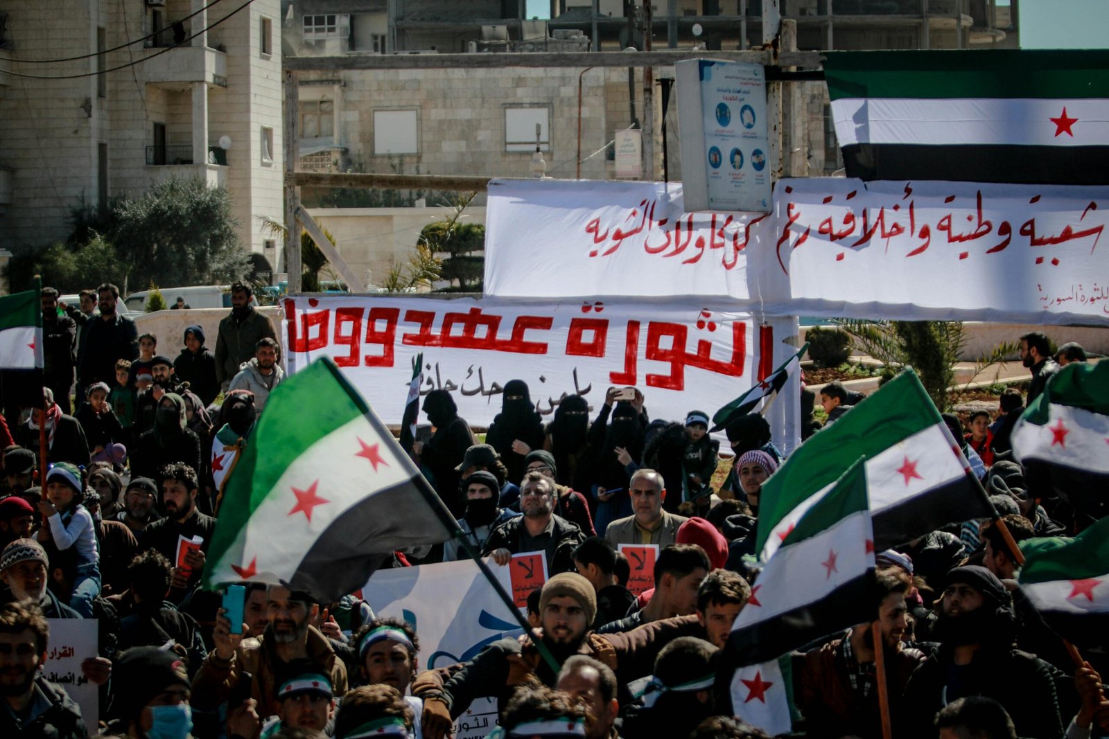 Crowd protests in Idlib, Syria with banners and flags, capturing a powerful moment.