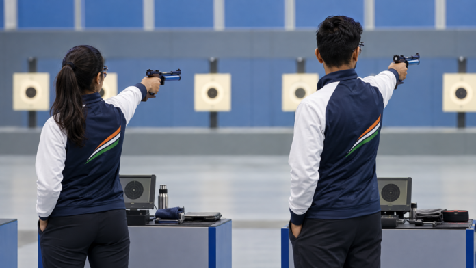 इनडोर रेंज में 10 मीटर एयर पिस्टल मिक्स्ड टीम स्पर्धा में निशाना लगाते भारतीय महिला और पुरुष खिलाड़ी