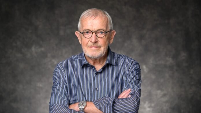 Portrait of physicist Francis Halzen, wearing glasses and a striped shirt, with his arms crossed