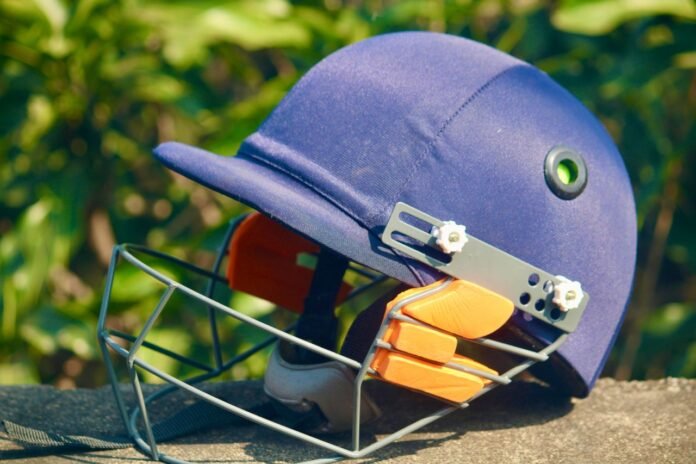 A blue cricket helmet placed outdoors with lush greenery in the background, showcasing sports equipment.